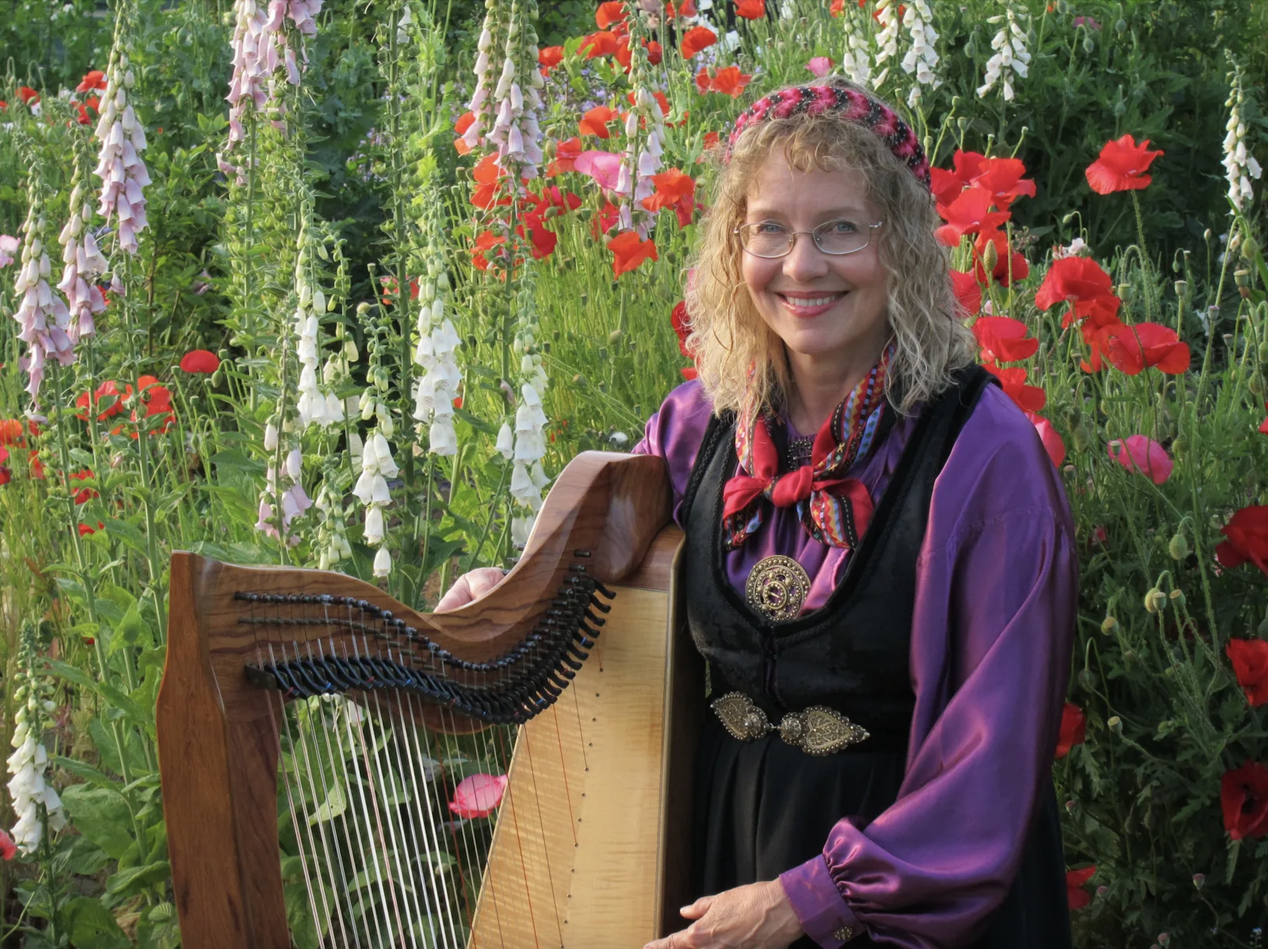 a woman in a nordic folk costume sits in a garden with a harp